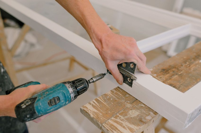 Cordless drill fastening a hinge to a white wood frame