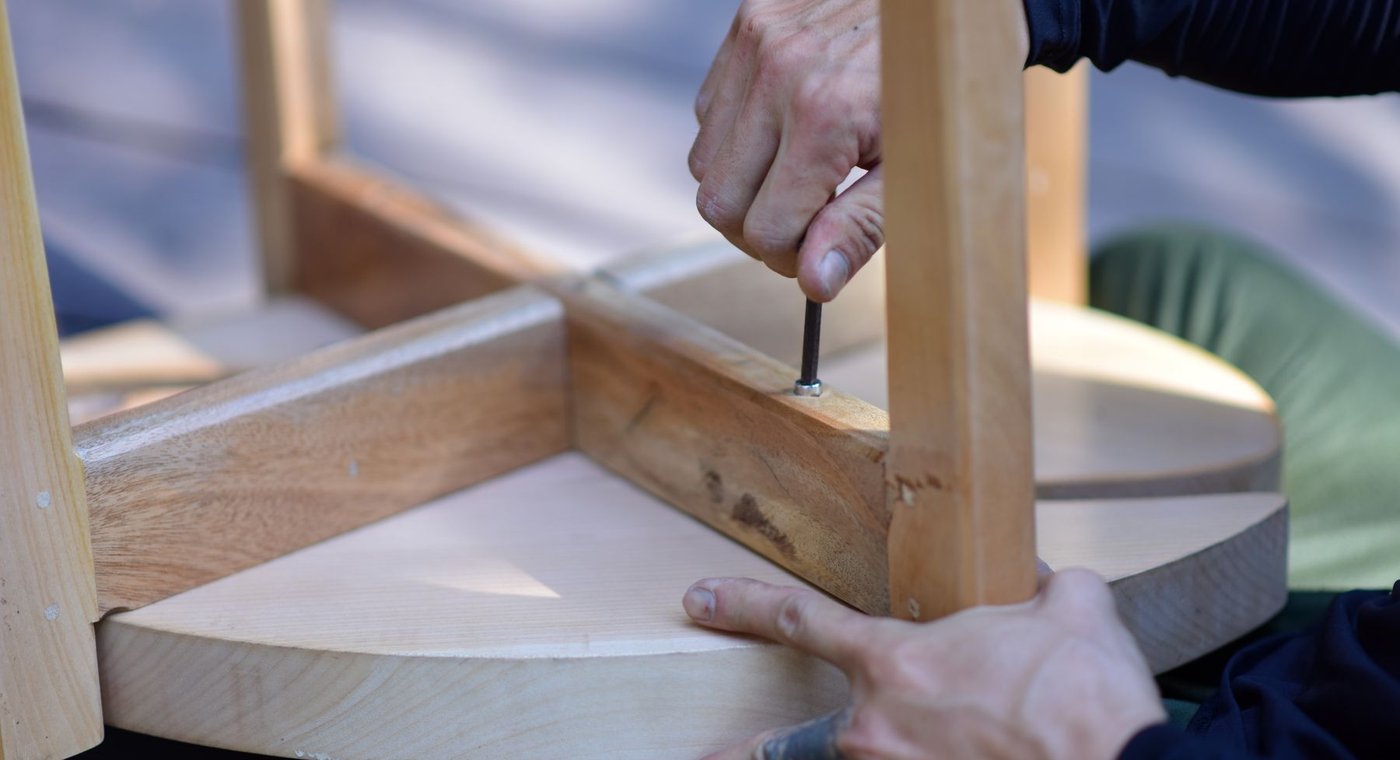 Hands driving a screw into the rail of a wooden stool being assembled