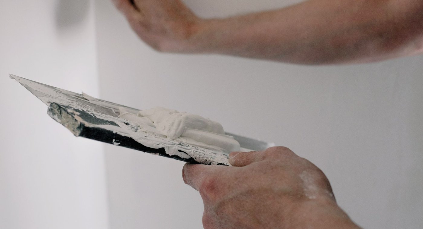 Two putty knives working joint compound into an inside corner of a wall